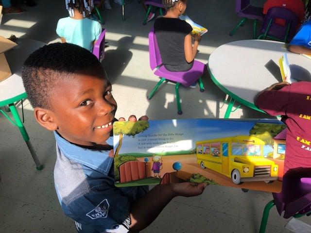 Young African American boy holding up Max Rhymes book proudly, learning reading skills, positive behavior, core values, self-respect, respect for others